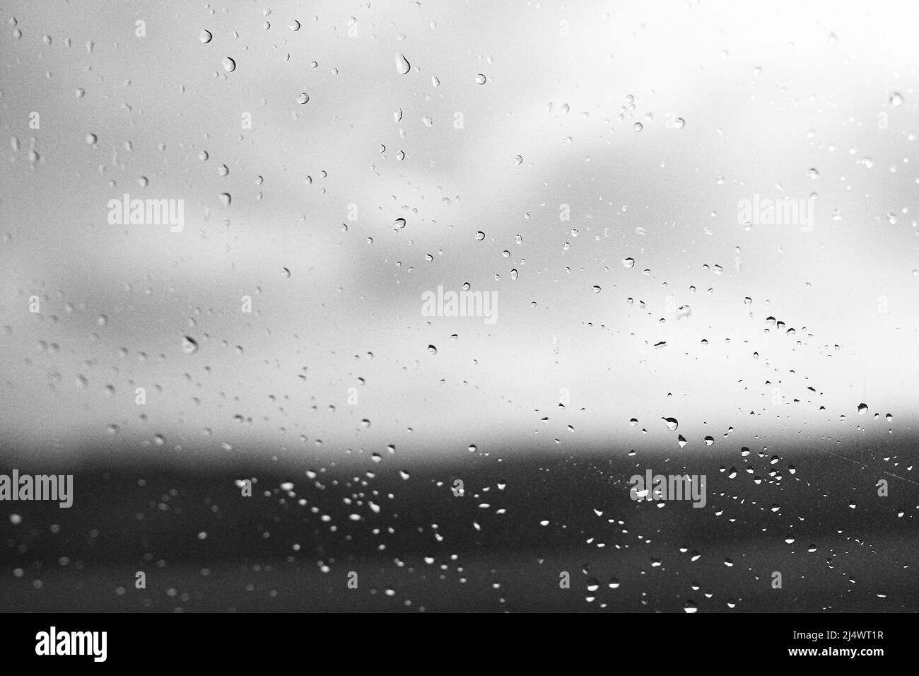 Gocce di pioggia sul vetro della finestra con sfondo sfocato in bianco e nero Foto Stock