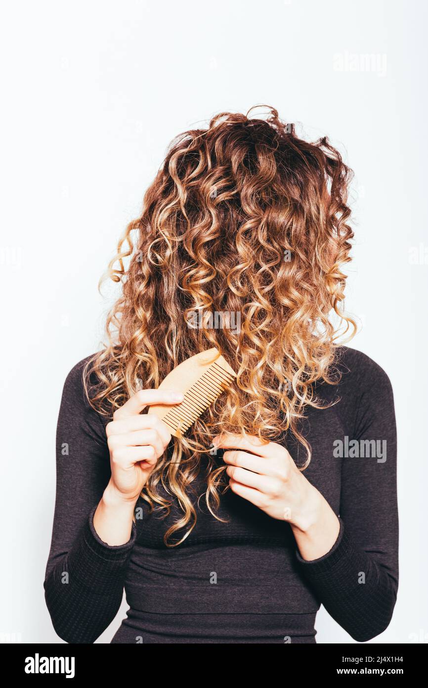 Giovane donna che pettina le punte aggrovigliate dei capelli ricci con un pettine di legno Foto Stock