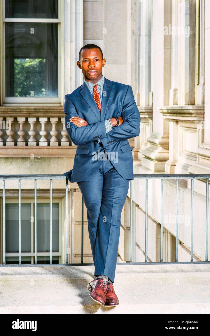 Uomo Urbano Moda. Vestirsi in abito blu, cravatta, scarpe in pelle, un  giovane uomo d'affari nero seduto su ringhiera in stile ufficio vintage  edificio, traversata Foto stock - Alamy