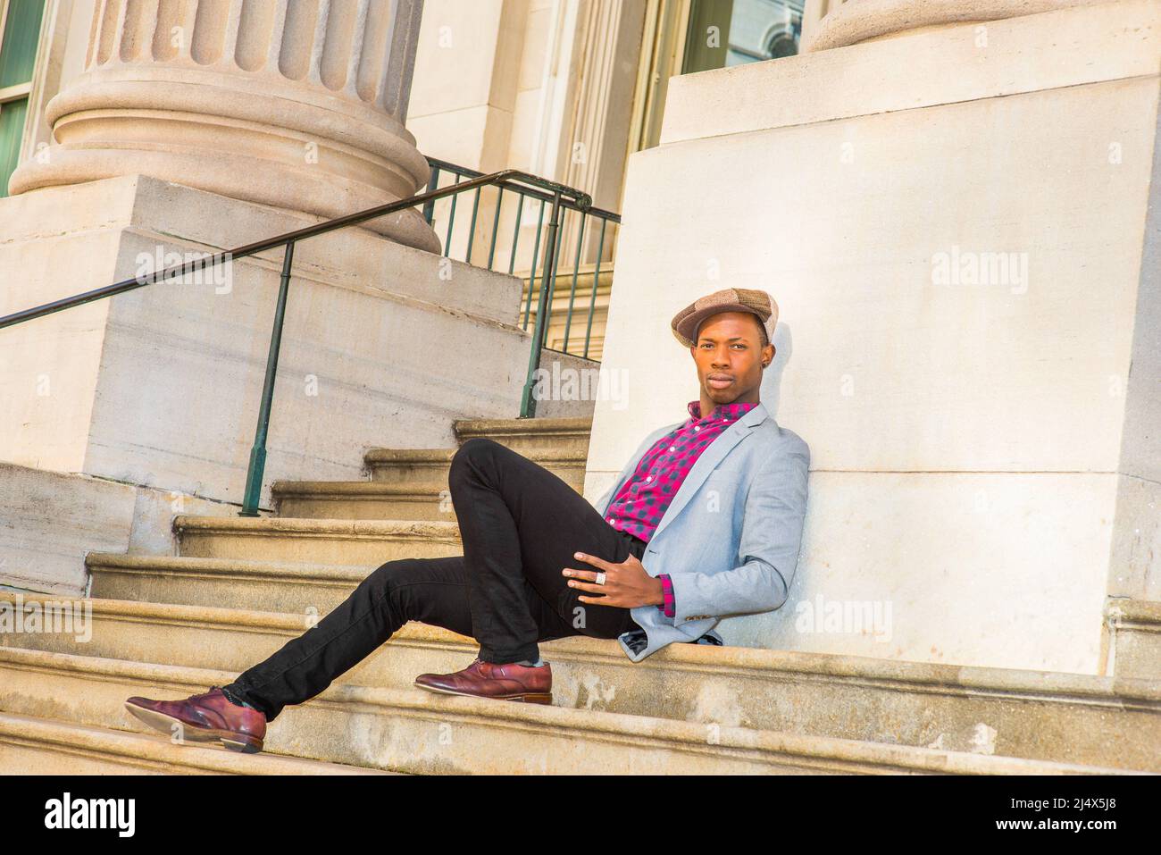 Uomo Urbano Moda. Indossare cappellino da edicola, vestirsi in blazer grigio chiaro, rosa a motivi geometrici, maglietta nera, pantaloni neri, scarpe in pelle marrone, un giovane bl Foto Stock