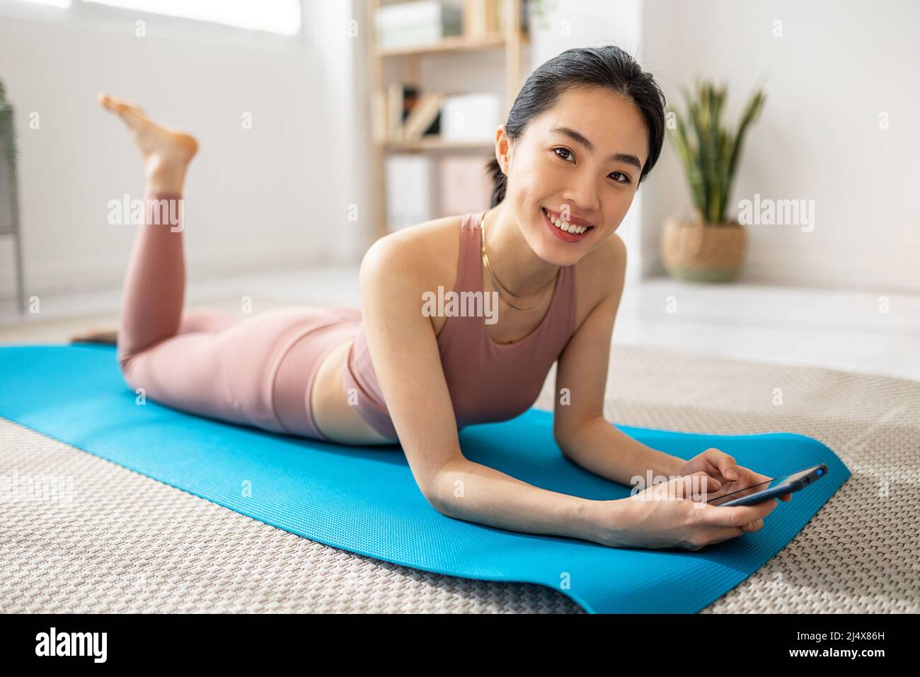 Sorridendo donna asiatica usando il telefono cellulare mentre si rilassa dopo l'allenamento Foto Stock