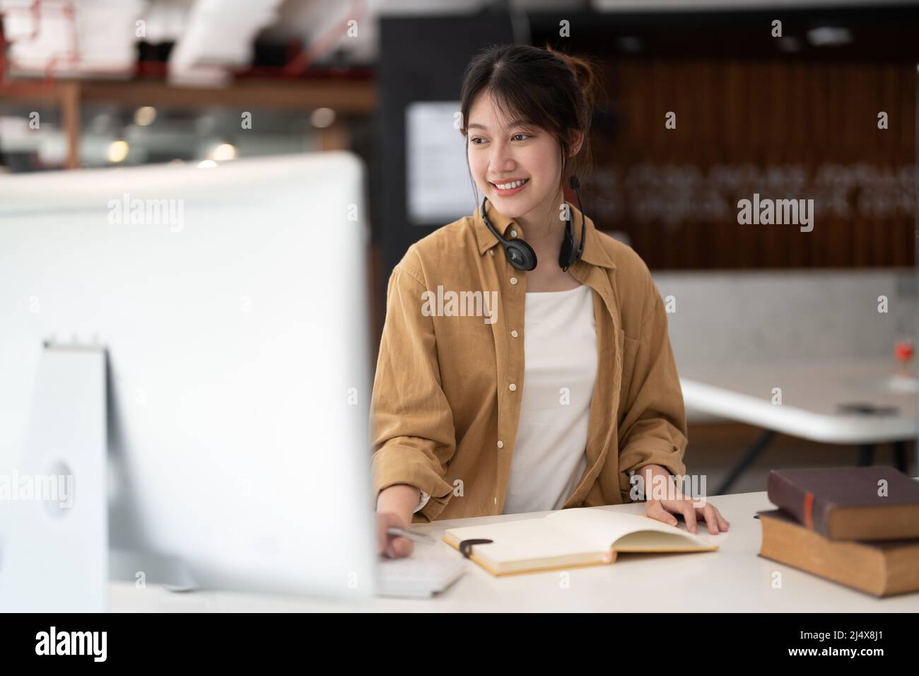 Hipster studente asiatico ragazza scuola con indossare cuffie scrivere note guardare video online webinar imparare su laptop sedersi a letto distanza corso di elearning Foto Stock