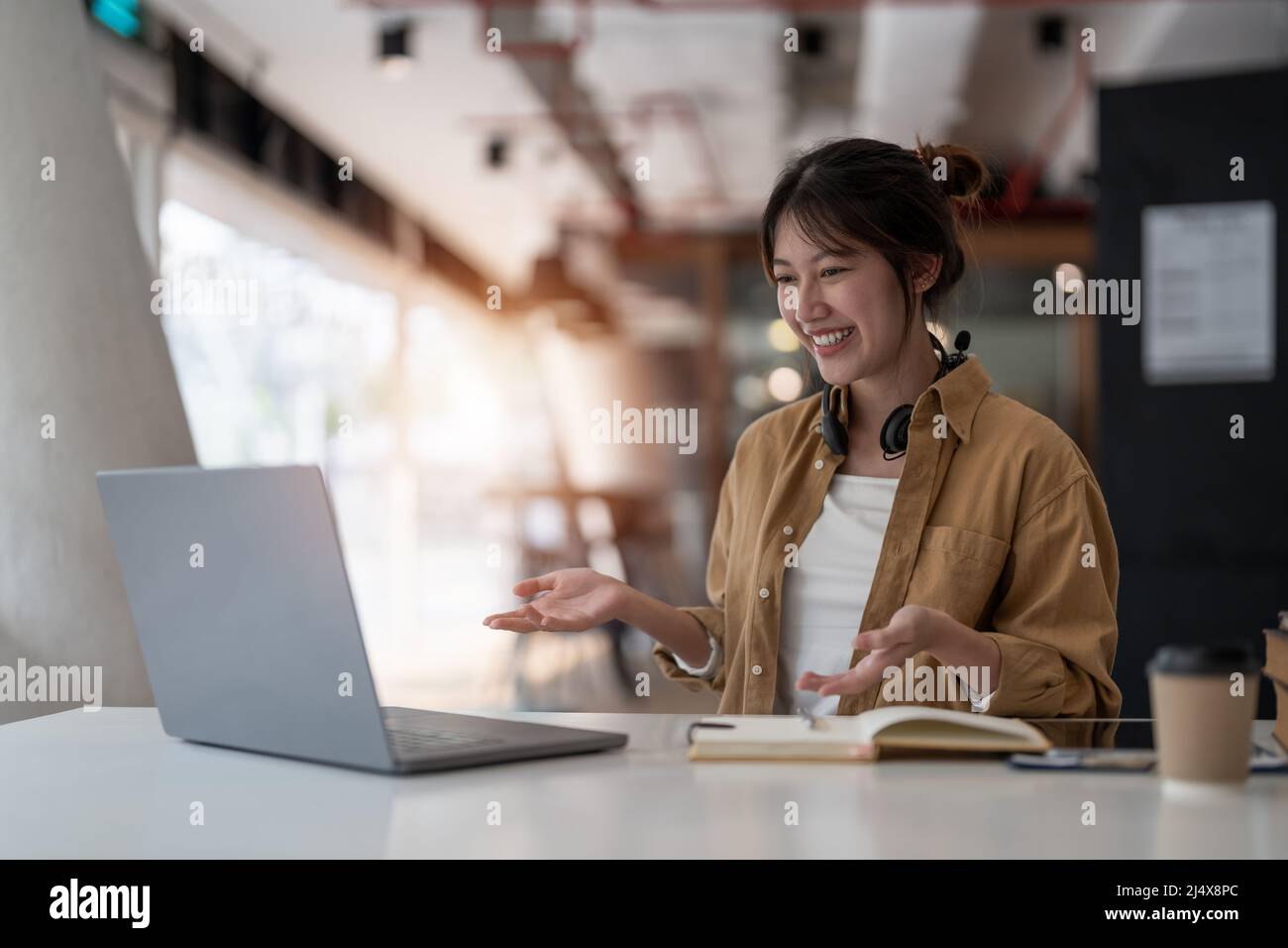 donna asiatica sorridente che indossa una cuffia, comunicando con il cliente tramite videochiamata. Millennial piacevole professionista tutor femminile Foto Stock