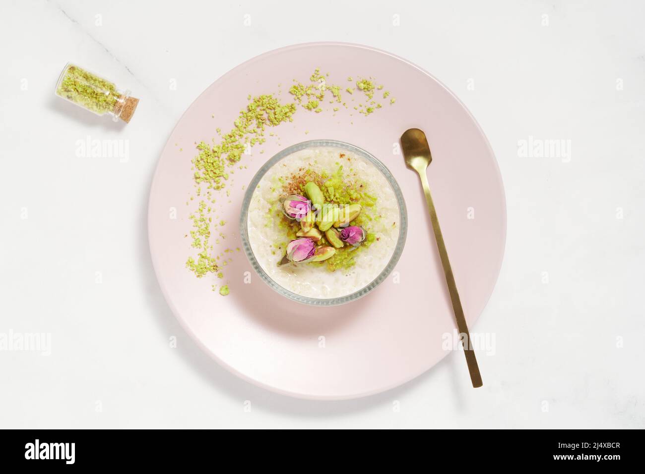 Dessert cremoso, budino di riso con pistacchio e cannella in una ciotola di vetro su tavola di marmo. Sfondo luminoso e arioso minimal. Vista dall'alto. Foto Stock