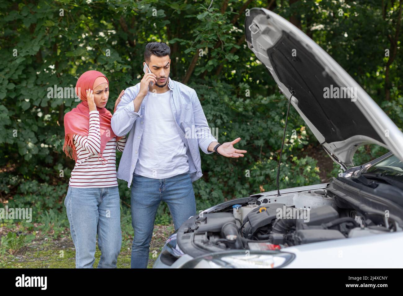 Triste despaired donna araba in hijab e l'uomo chiamata al supporto auto, stare vicino a macchina rotta con cofano aperto Foto Stock