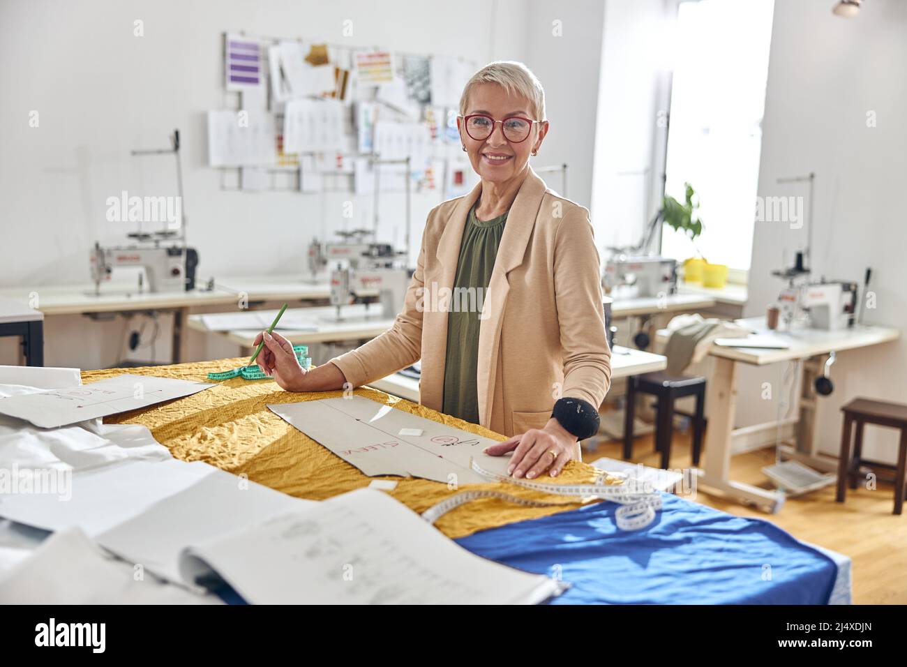 Ritratto di donna abiti designer in elegante giacca si trova sul posto di lavoro confortevole Foto Stock