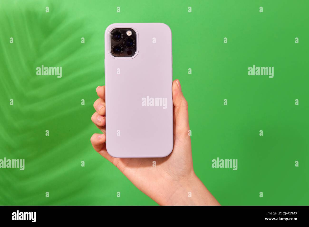 Smartphone bianco femmina con custodia in morbido silicone, vista posteriore . Custodia del telefono mock in su isolato su sfondo verde ombra da una pianta Foto Stock