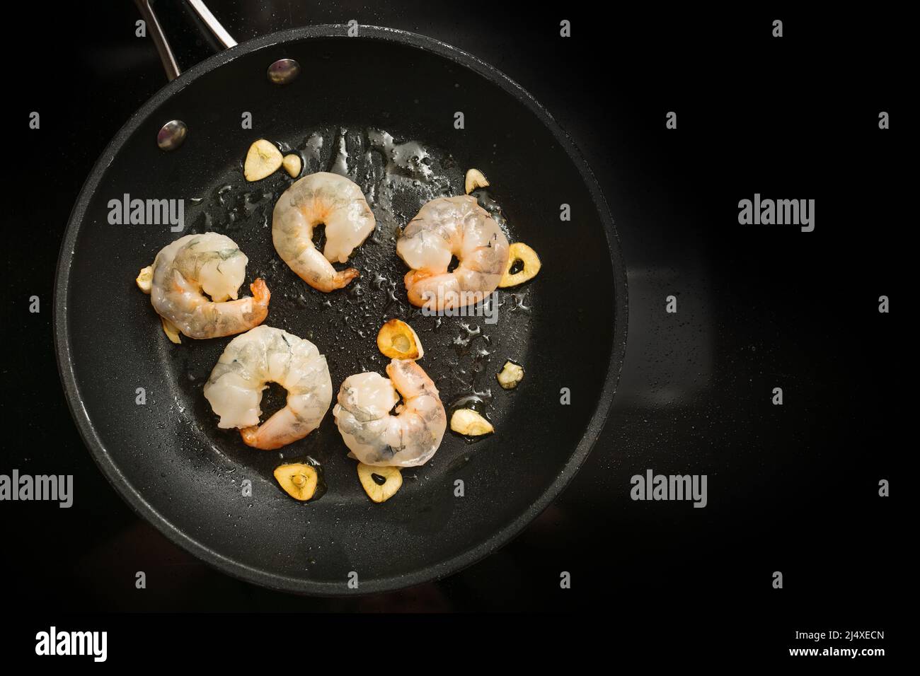 I gamberetti freschi vengono saltati con aglio in olio d'oliva in una pentola di cottura sul fornello nero, preparazione per un delizioso antipasto, spazio copia, angolo alto Foto Stock