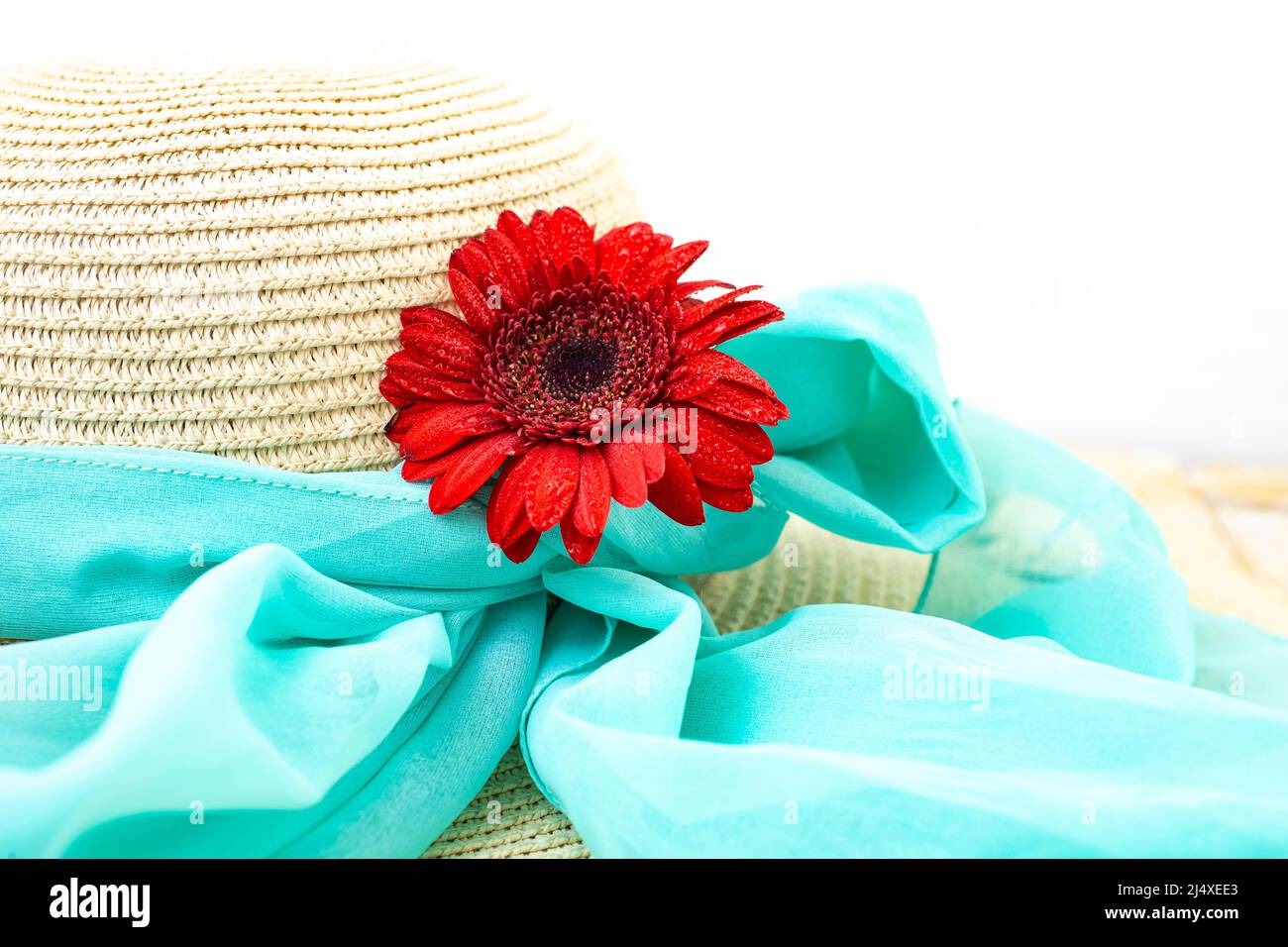 Rosso gerbera margherita fiore su un cappello di paglia legato con una sciarpa blu, estate , spiaggia, sfondo romantico Foto Stock