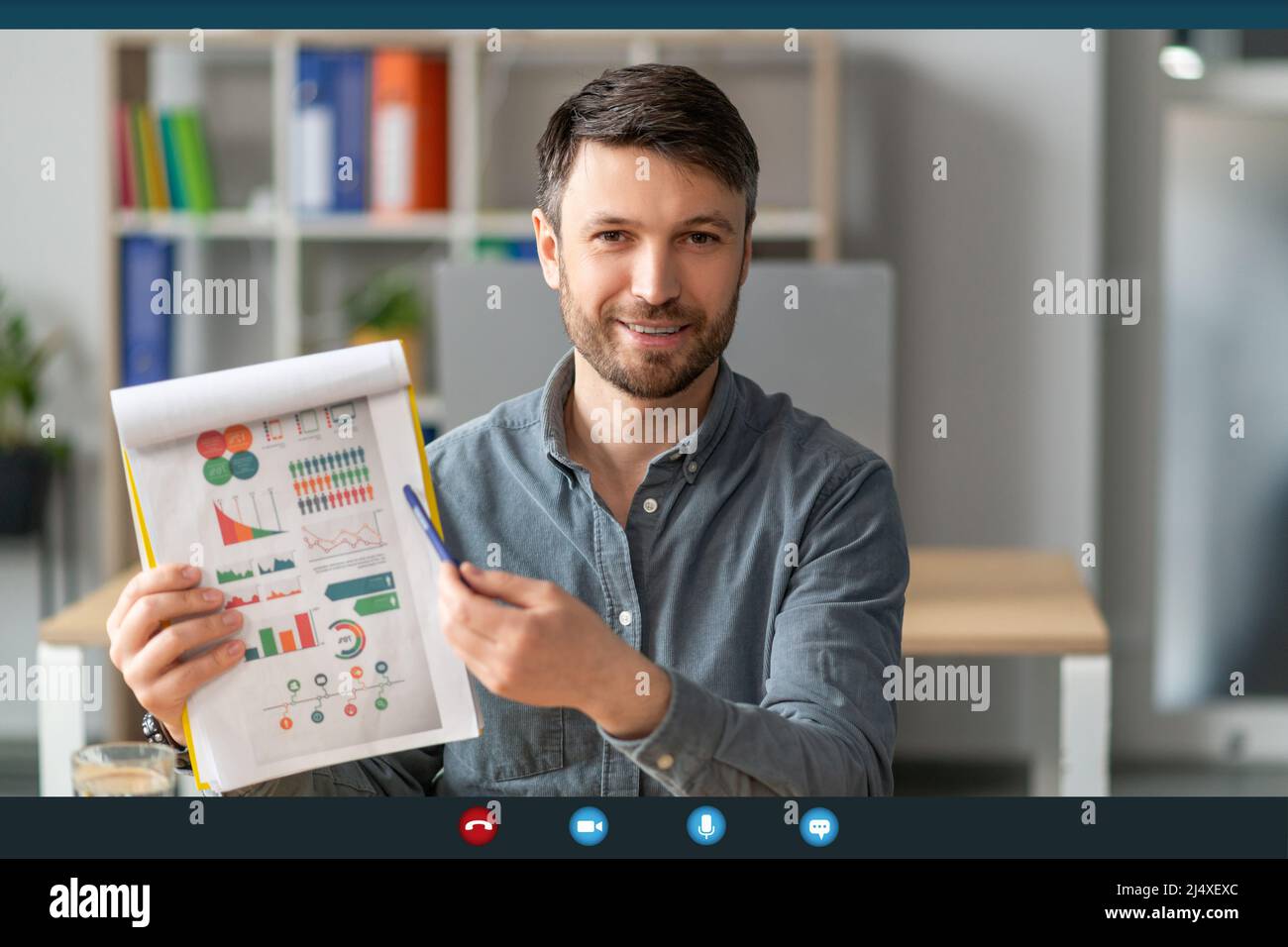 Imprenditore maschio maturo che mostra i rapporti alla webcam durante la conferenza online di affari in ufficio, monitorare screenshot Foto Stock