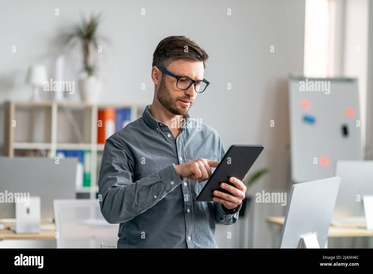 Tecnologie moderne nel business. Concentrato uomo d'affari maturo che utilizza tablet digitali in ufficio Foto Stock