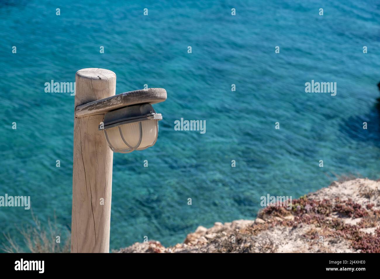 Lampione, palo in legno con lampada in terra rocciosa, sfocatura sfondo del mare Egeo, estate giorno di sole. Isola di Koufonisia, Cicladi, Grecia. Vista dall'alto Foto Stock