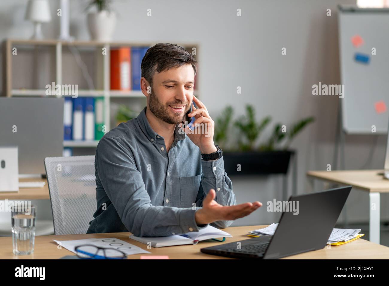 Uomo d'affari felice maturo che parla sul cellulare, discute di domande di lavoro, guarda il laptop, seduto sul posto di lavoro Foto Stock