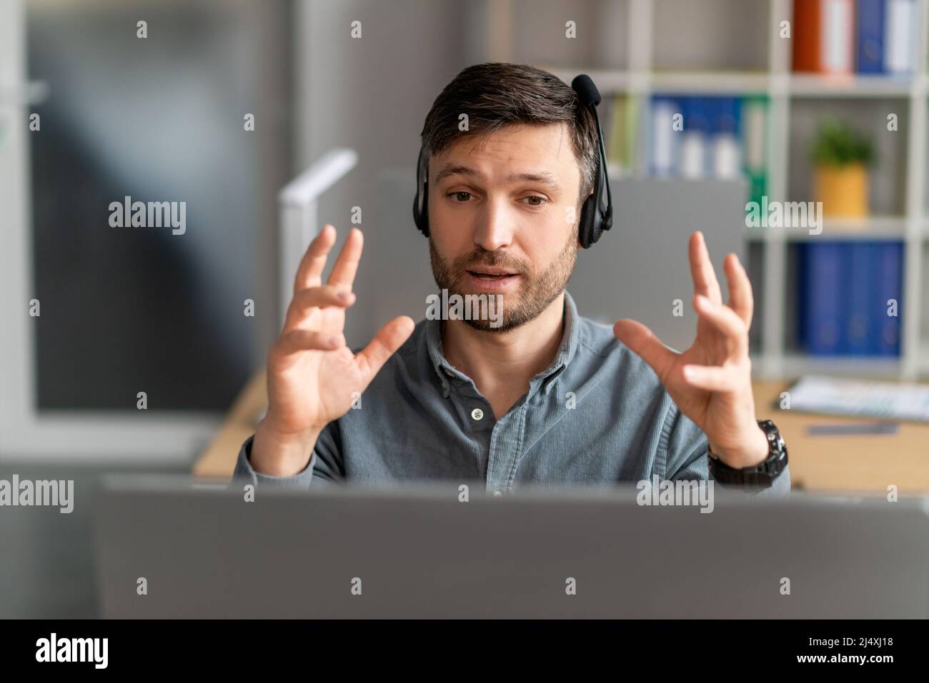 Ritratto di un manager maschile concentrato in cuffia con chiamata Web su pc seduto alla scrivania sul posto di lavoro, spiegando la strategia Foto Stock