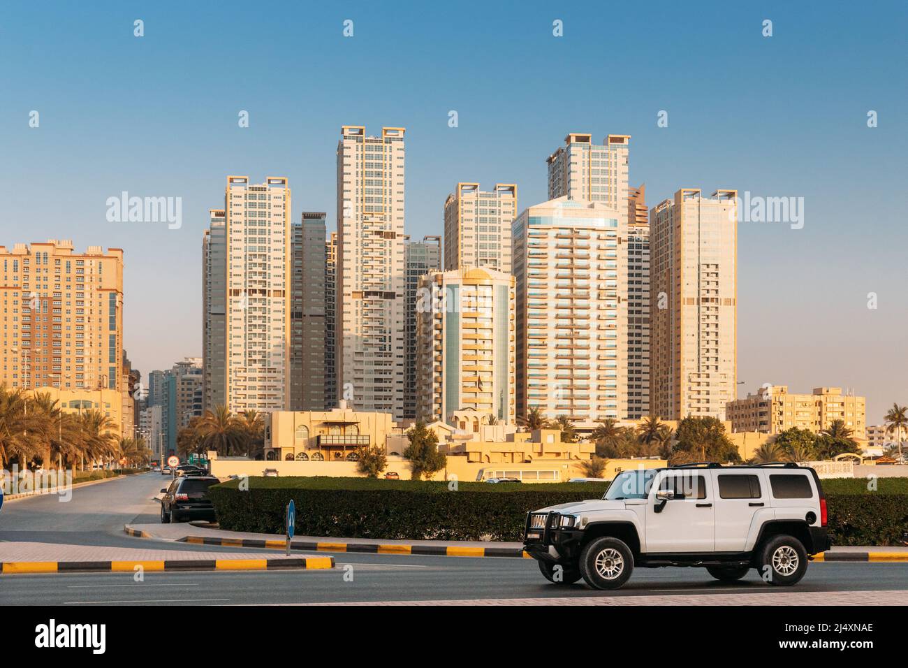 White SUV Car in movimento in City Street. Nuove case residenziali a più piani. Skyline della città in Sunny Spring sera su Blue Sky. Immobiliare Foto Stock
