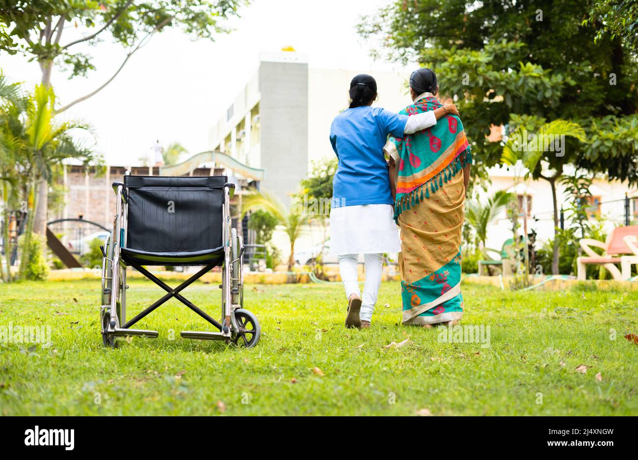 Focus su poltrona, infermiera a piedi sostenendo anziana donna anziana da sedia a rotelle - concetto riabilitazione, custode e trattamento medicare Foto Stock