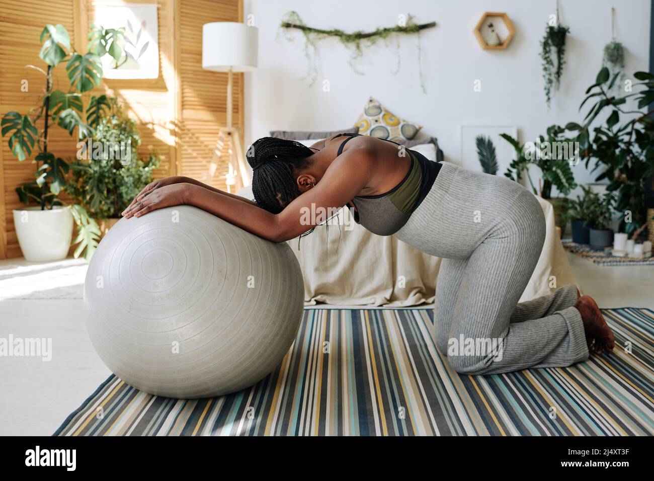 Donna incinta africana in piedi sulle ginocchia appoggiata sulla sfera di idoneità che sente dolore durante le contrazioni, che dà alla luce a casa Foto Stock