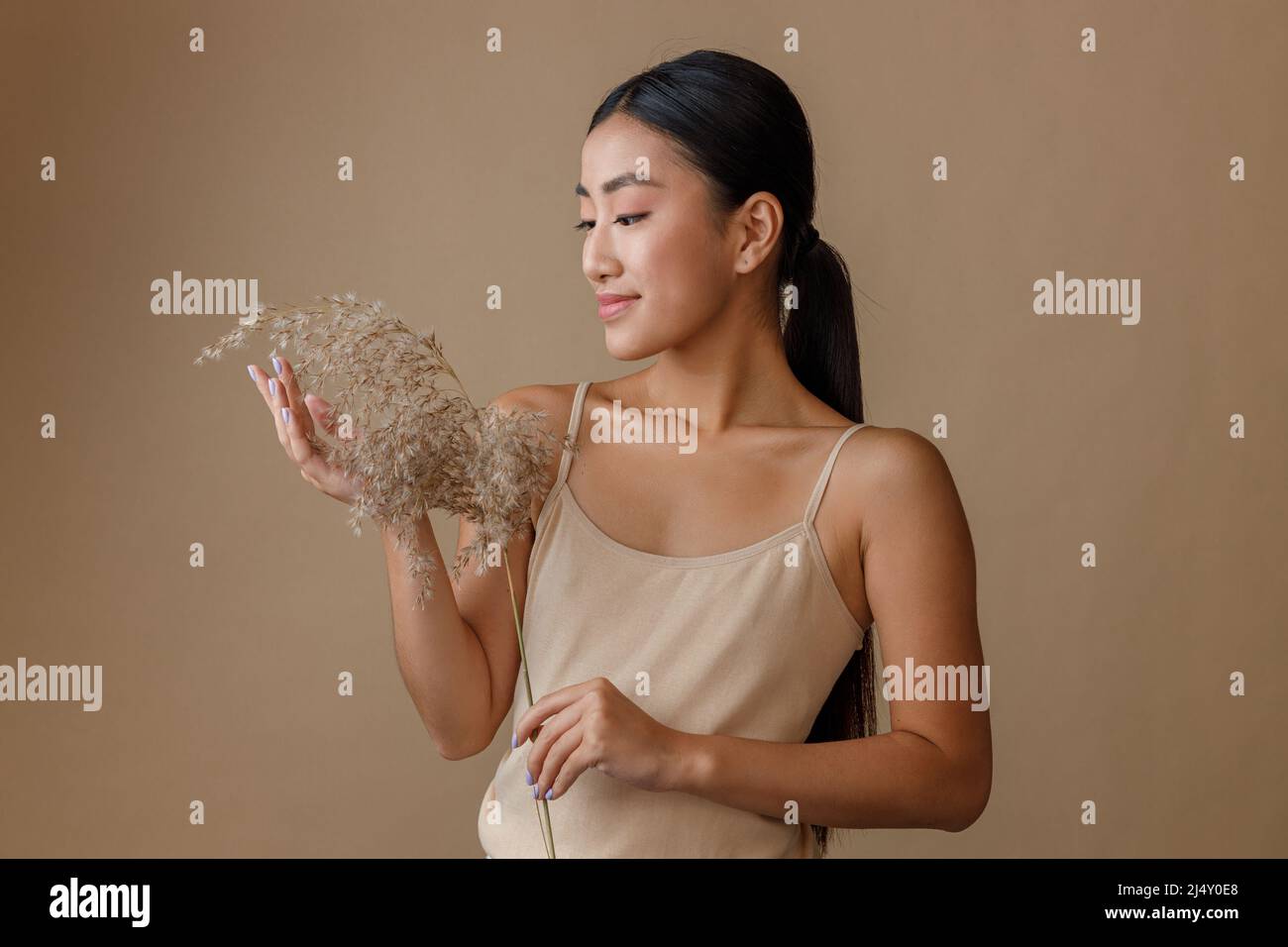 Giovane donna asiatica con erba di cereali in piedi in studio Foto Stock