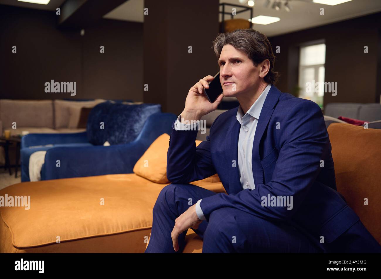 Ritratto di un bel uomo europeo maturo in tuta aziendale, cliente acquirente parlare sul telefono cellulare mentre si visita un negozio di mobili e testin Foto Stock
