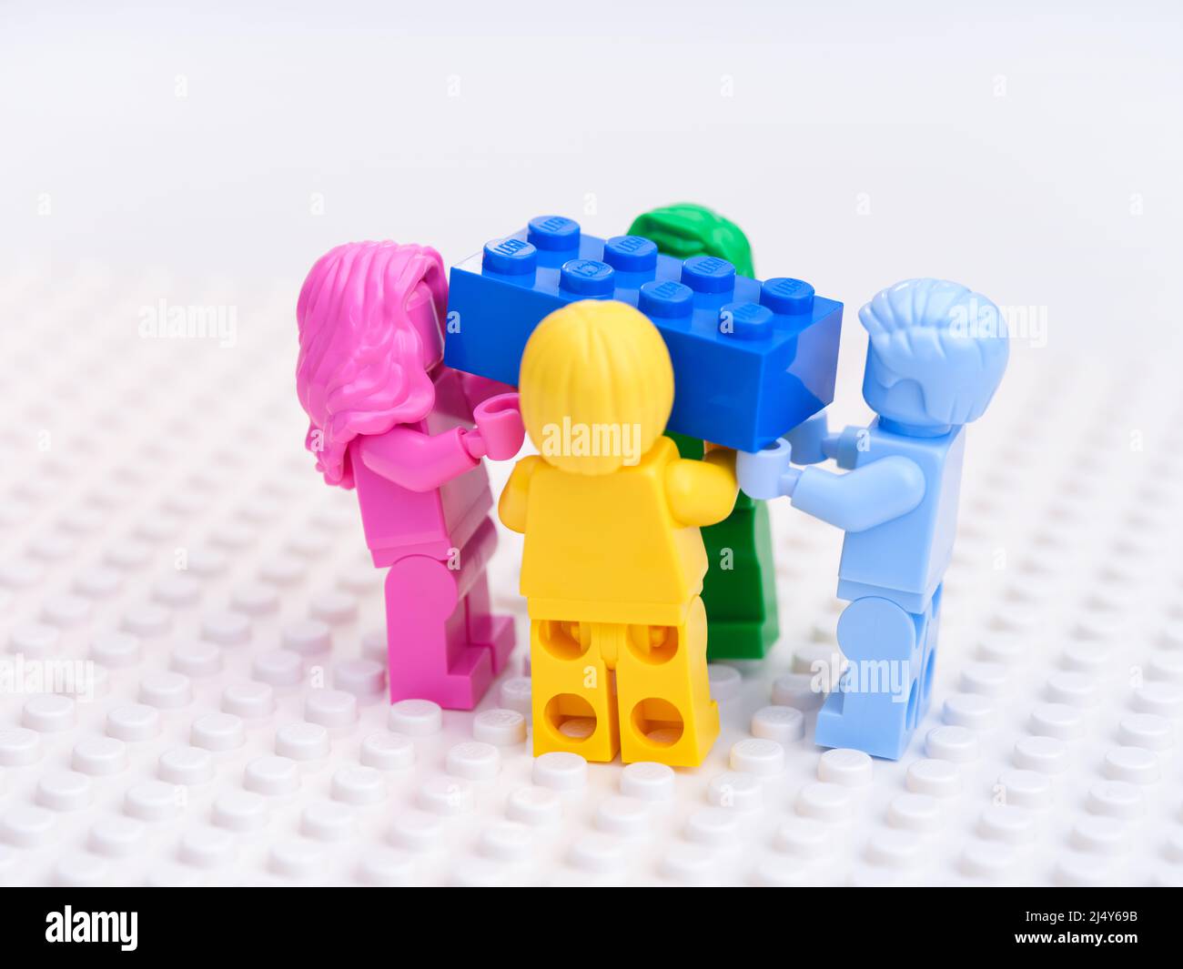 Tambov, Federazione Russa - 17 ottobre 2021 quattro minifigure Lego monocromatiche che trasportano un mattone Lego blu su uno sfondo bianco della piastra di base. Foto Stock