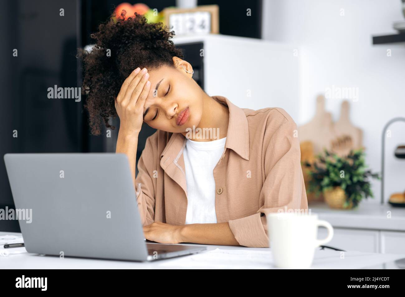 Stanco superlavorato african american millennial bella ragazza, studente, freelancer, stanco di lavoro remoto o di studio, chiuso gli occhi, si addormenta durante il lavoro, ha bisogno di sonno, riposo, caffè Foto Stock