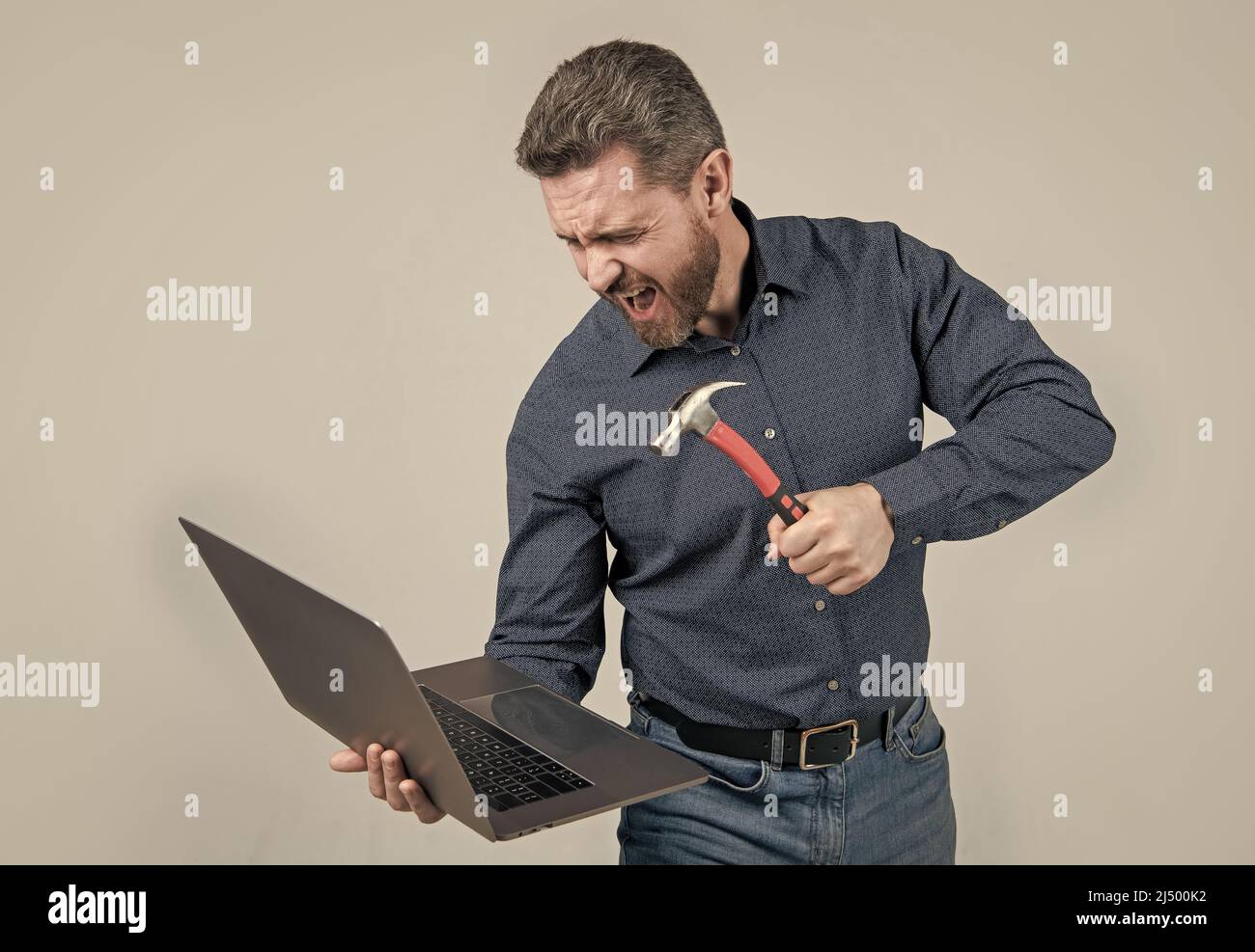 Furious uomo rompere notebook colpire notebook con sfondo grigio martello, computer rabbia Foto Stock