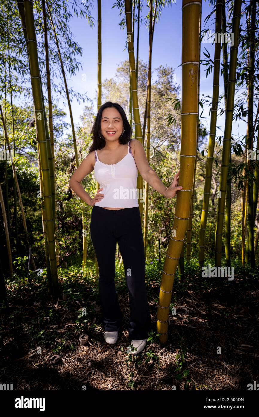 Giovane donna asiatica in casual abiti Springtime in piedi in un grande boschetto di bambù Foto Stock