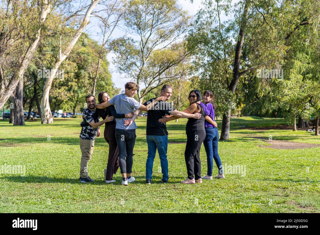 Gruppo multietnico di famiglia che cammina braccio in braccio in un parco, guardando la macchina fotografica sorridente, felice atteggiamento. Famiglia, gruppo, lavoro di squadra, concetto di amicizia Foto Stock
