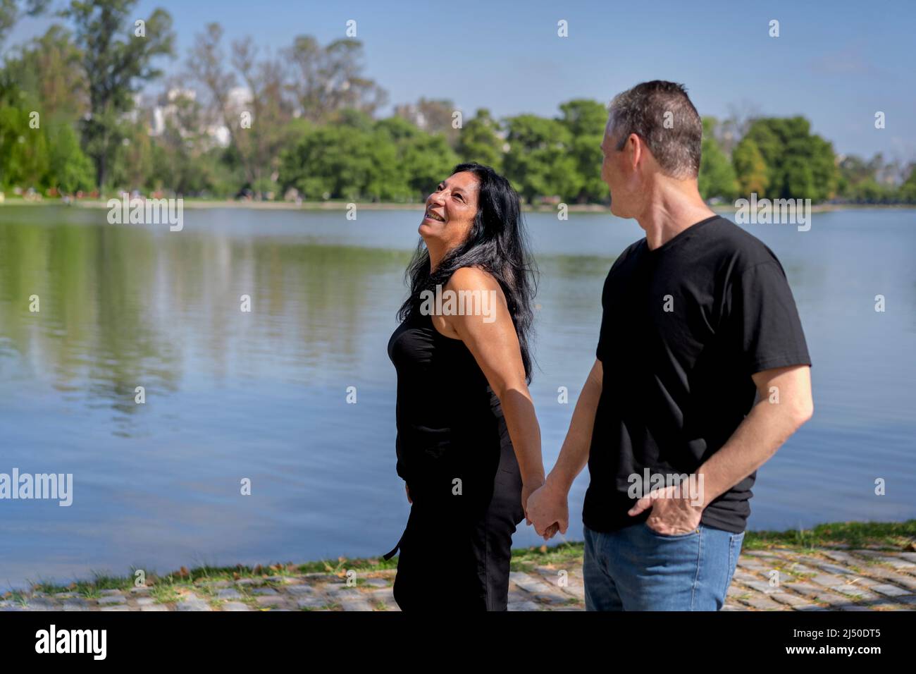 Coppia multietnica formata da una donna andina e da un uomo caucasico che cammina accanto ad un lago. Espressioni felici e volti di amanti Foto Stock