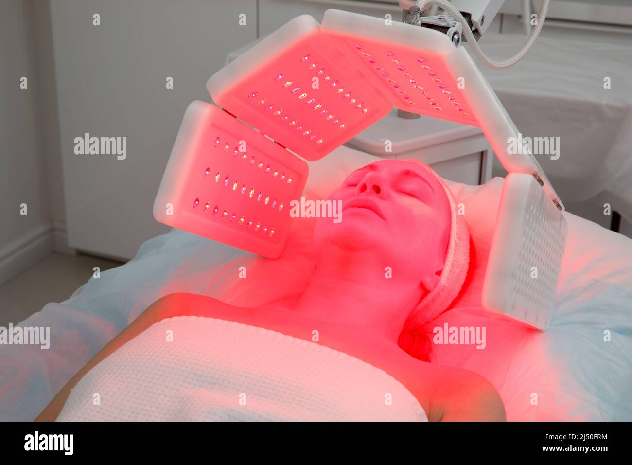 Una donna anziana subisce una procedura di ringiovanimento facciale. Donna viso lt trattamento luce rossa presso la clinica di bellezza. Cosmetologia. Foto Stock