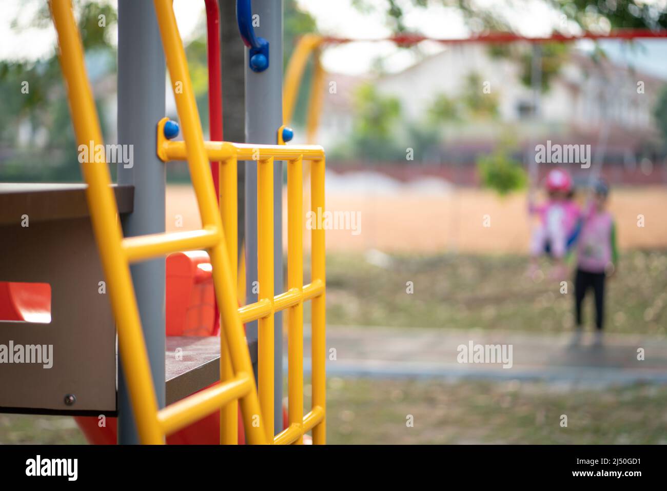 Attrezzature per giochi per bambini, con bambini fuori fuoco che giocano sull'altalena in background. Foto Stock