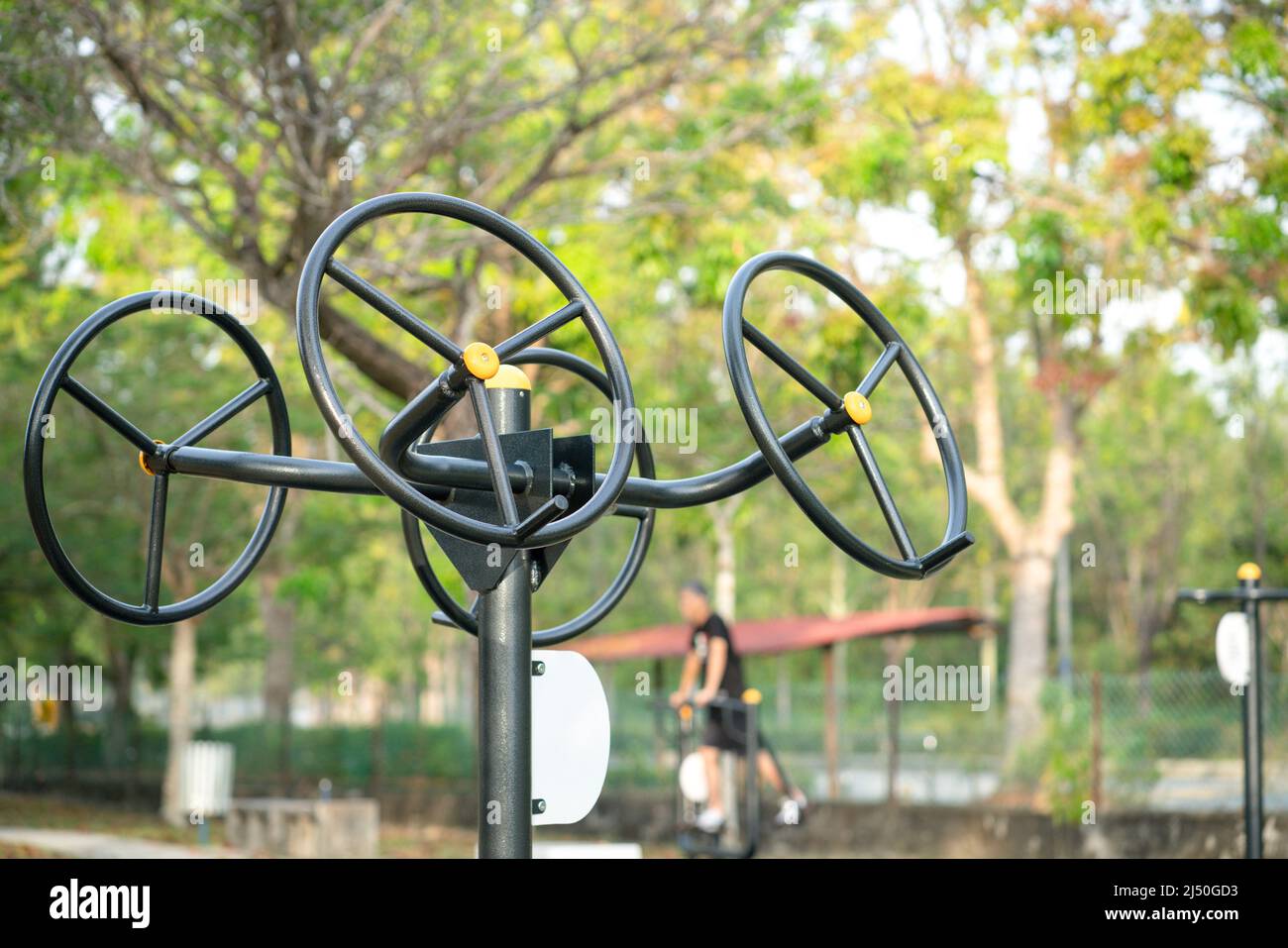 Attrezzature per esercizi o fitness, ruota di stretching doppia nel parco, con l'uomo fuori fuoco che si esercita in background. Foto Stock