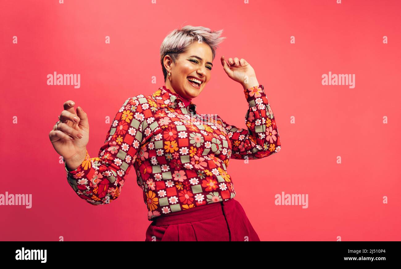 Sensazione di vitalità ed energia. Felice giovane donna che balla e sorride allegro mentre si alza su uno sfondo rosso. Giovane donna con capelli tinti ha Foto Stock