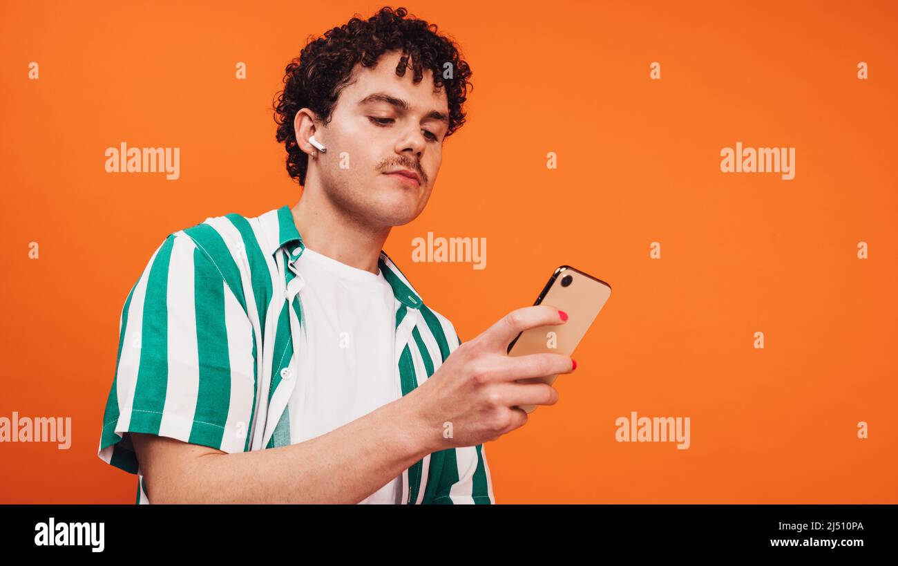 Navigare in rete per una musica vivace. Uomo in attesa sicuro che utilizza uno smartphone mentre indossa le cuffie wireless. Giovane uomo non conforme che ascolta il suo Foto Stock