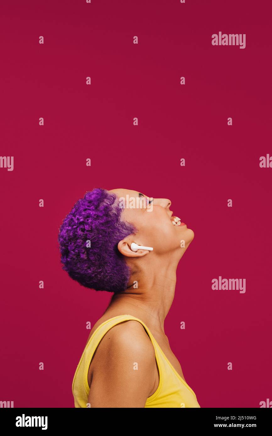 Goditi al massimo la musica. Spensierate la giovane donna che ascolta la musica con le sue cuffie wireless. Donna con capelli viola sorridente allegro mentre stan Foto Stock