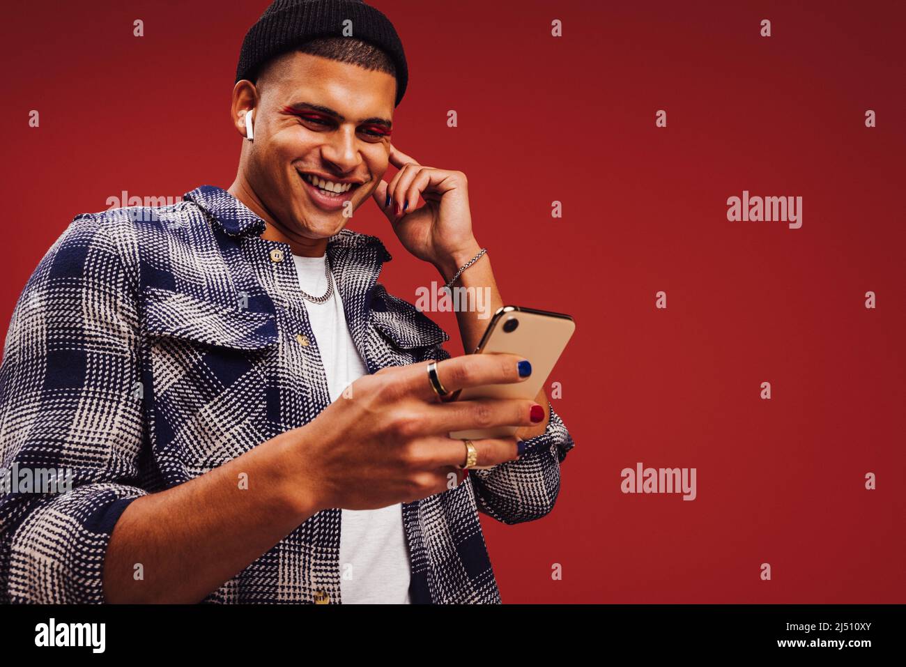 Giovane che riproduce in streaming i suoi elenchi di riproduzione preferiti. Buon giovane uomo sorridente allegro mentre tiene uno smartphone e indossa le cuffie wireless. Alla moda Foto Stock