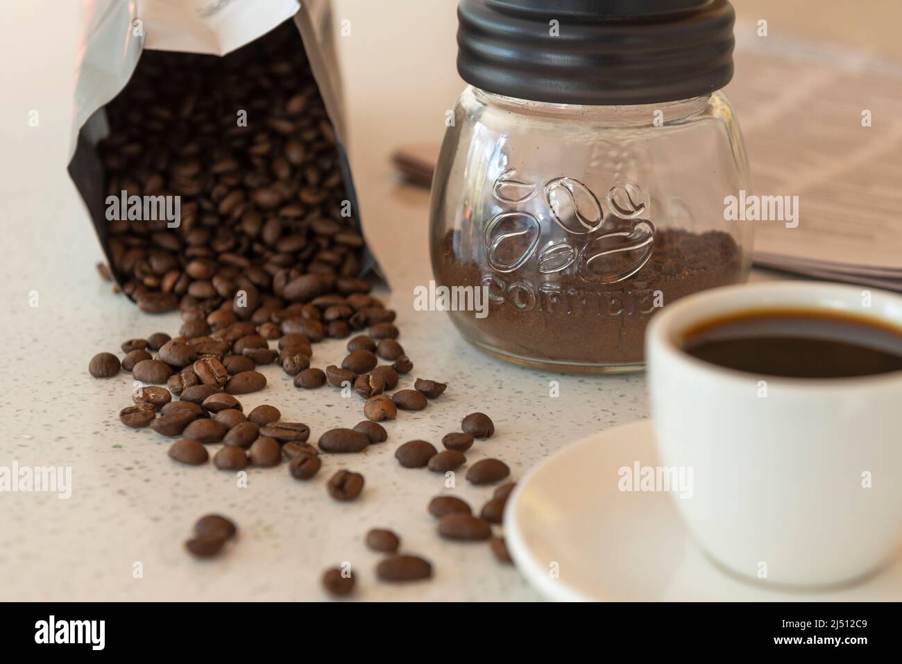 I chicchi di caffè fuoriesca dal loro pacchetto su un banco con una tazza di caffè e caffè macinato nelle vicinanze. Foto Stock