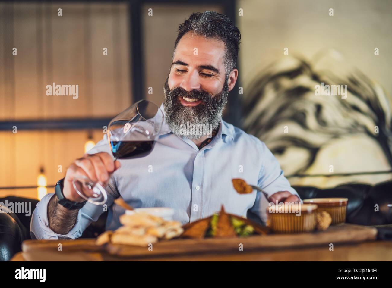 L'uomo adulto felice sta mangiando e mangiando vino al ristorante. Foto Stock