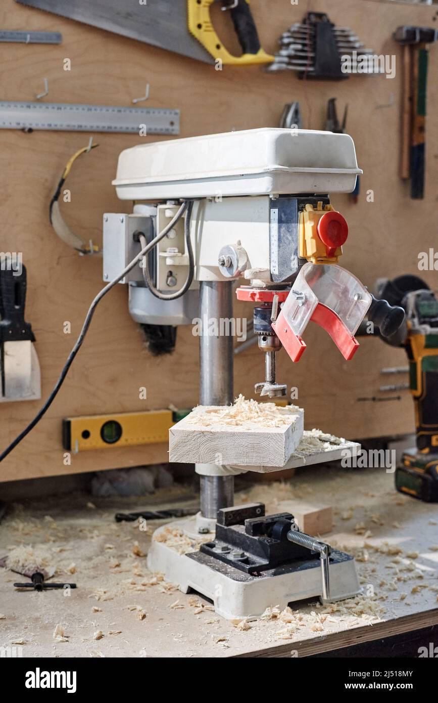Verticale nessuna figura della moderna pressa a forare sul tavolo con altri utensili a parete in officina di lavorazione del legno Foto Stock