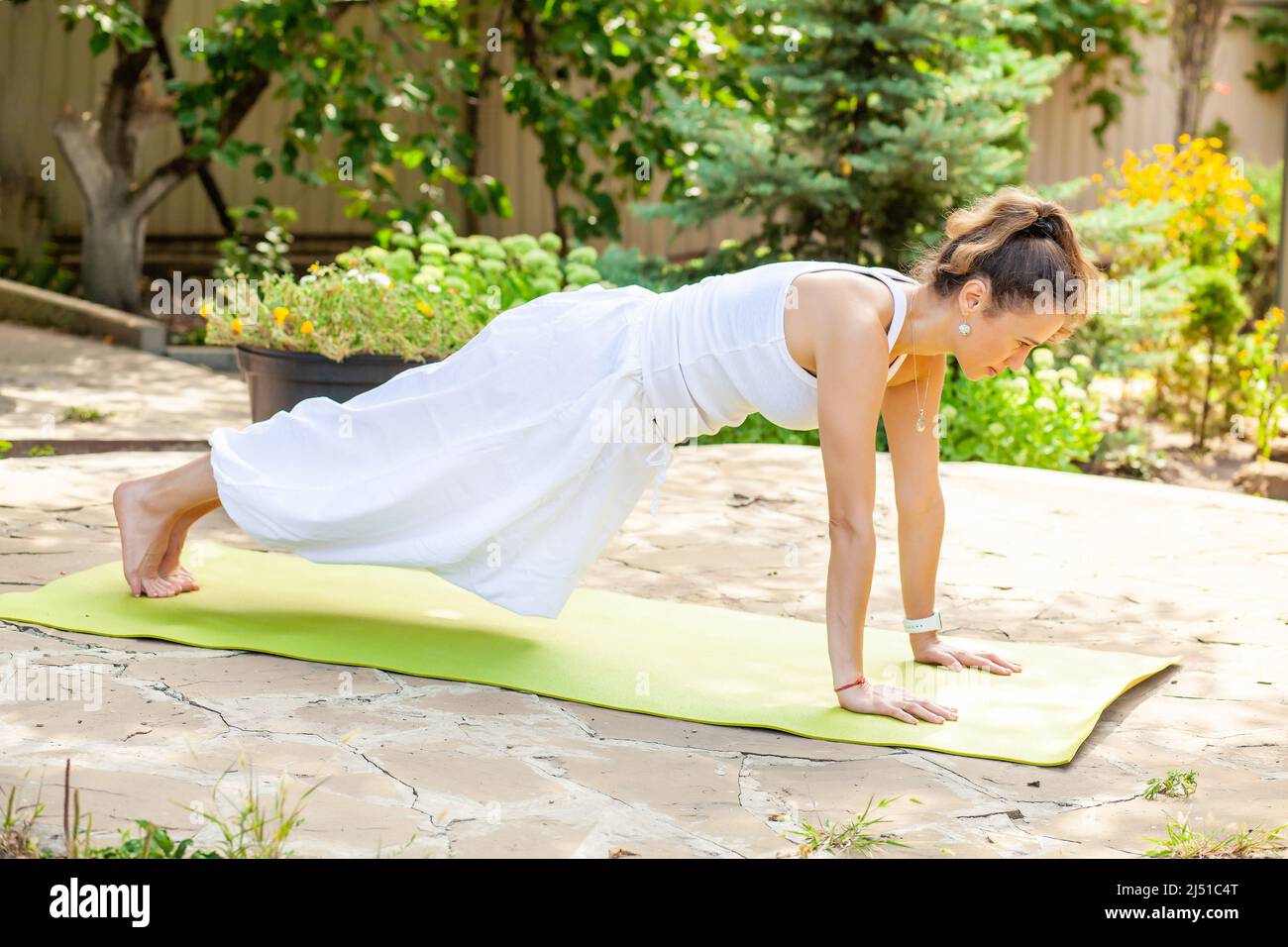 La giovane donna pratica lo yoga in giardino. Surya namaskar, esercitazione del gambo. Upper chaturanga dandasana, Kumbhakasana - la posa della tavola Foto Stock