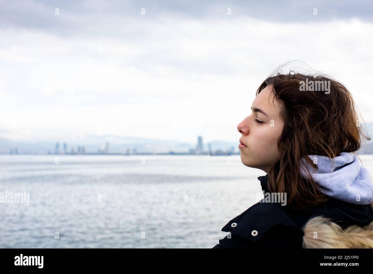 Giovane ragazza pensiva che guarda al mare dalla barca. Ragazza adolescente a ferry boat. Mare grigio freddo Foto Stock