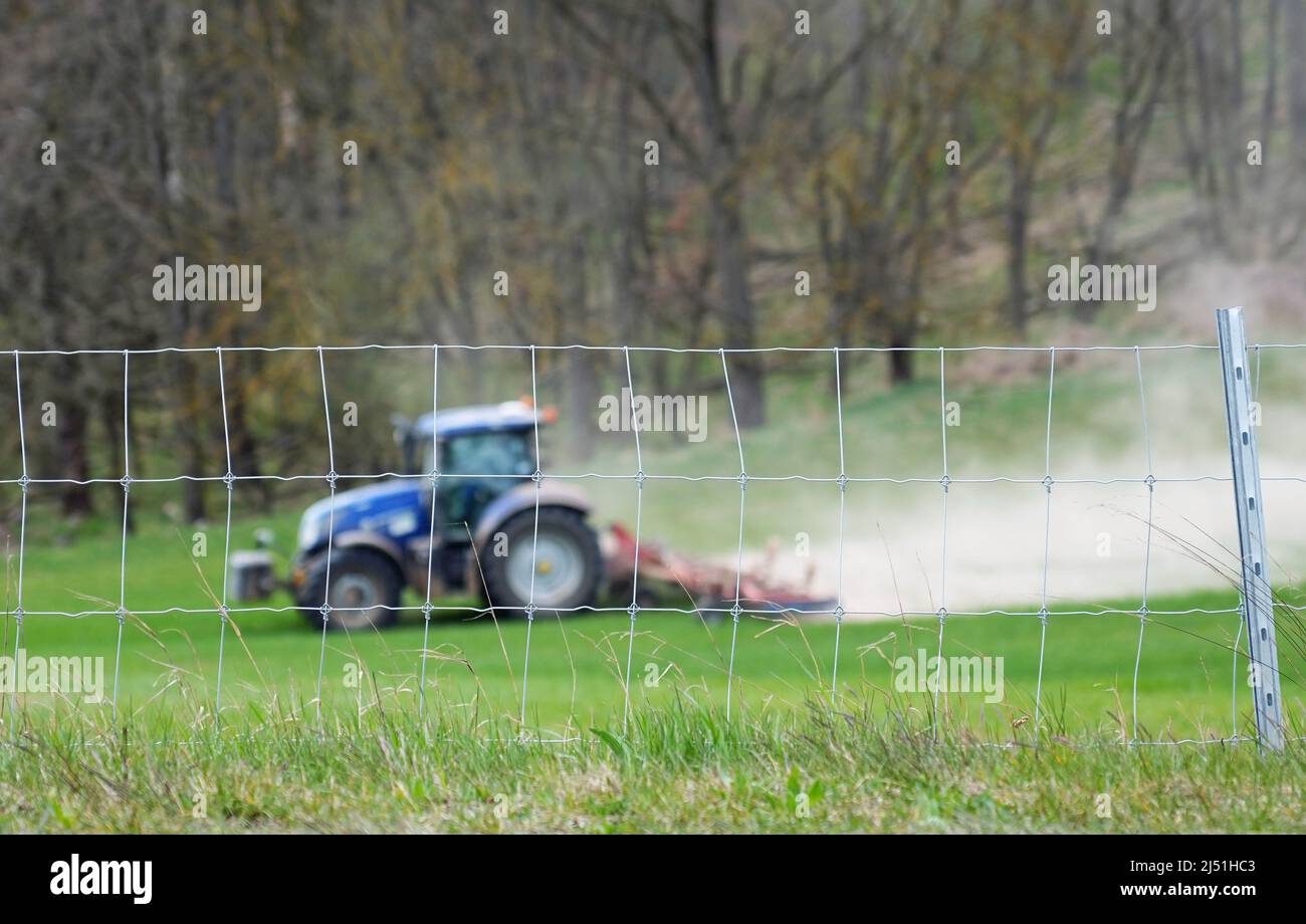 19 aprile 2022, Brandeburgo, Schwedt/OT Criewen: Un agricoltore guida il suo trattore in un campo nel Parco Nazionale della bassa Oder Valley; in primo piano è la recinzione di protezione contro la diffusione della peste suina africana (ASF) di nuova costruzione. Dopo le critiche sul percorso precedente, la recinzione fissa vi è stato spostato ad ovest su una lunghezza di circa undici chilometri.la demolizione della vecchia recinzione, che è stata parzialmente sommersa in acqua, è iniziata. Foto: Soeren Stache/dpa Foto Stock