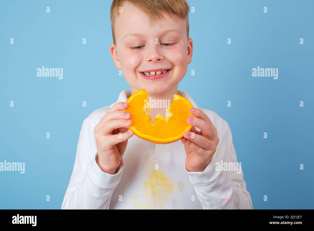 Ragazzo che tiene una metà tagliata di un arancio. Macchie sporche di succo d'arancia sui vestiti. Il concetto di pulizia delle macchie sui vestiti Foto Stock