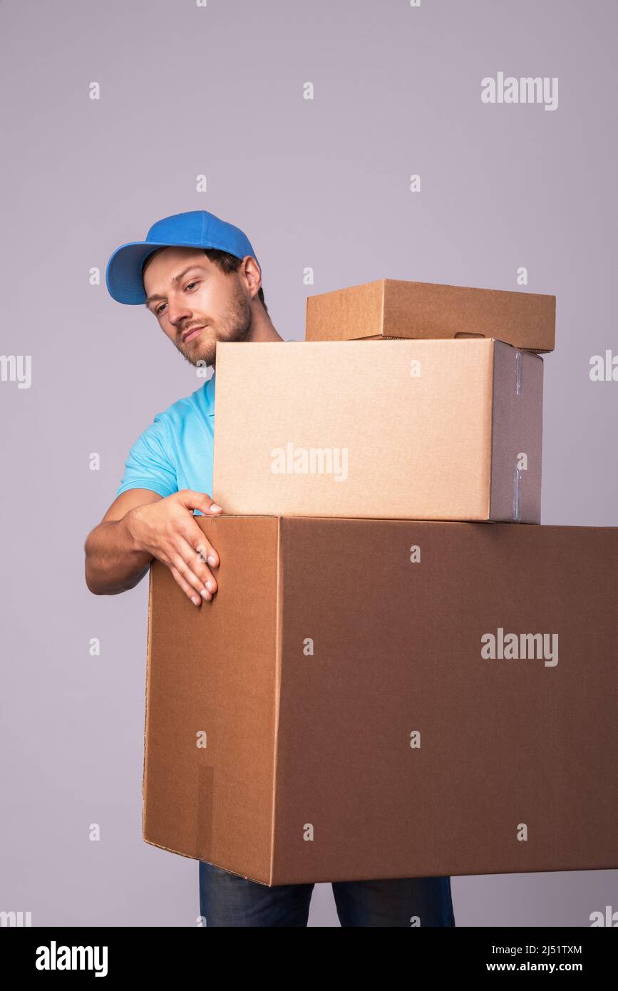 Uomo felice di consegna durante il lavoro con un imballaggio in scatole di cartone su sfondo grigio Foto Stock