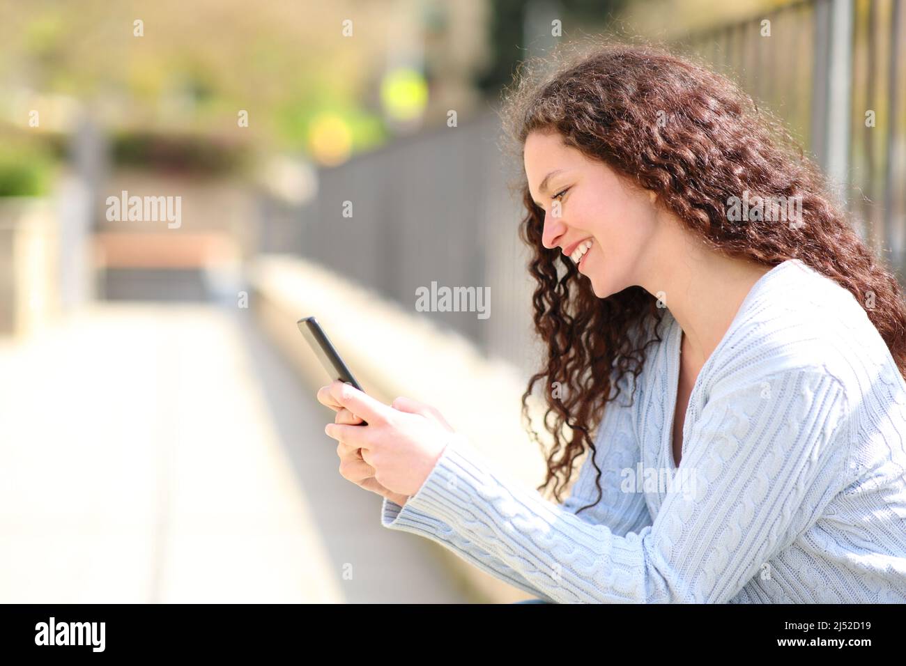 La vista laterale ritratto di una donna felice sta usando uno smartphone in un parco Foto Stock