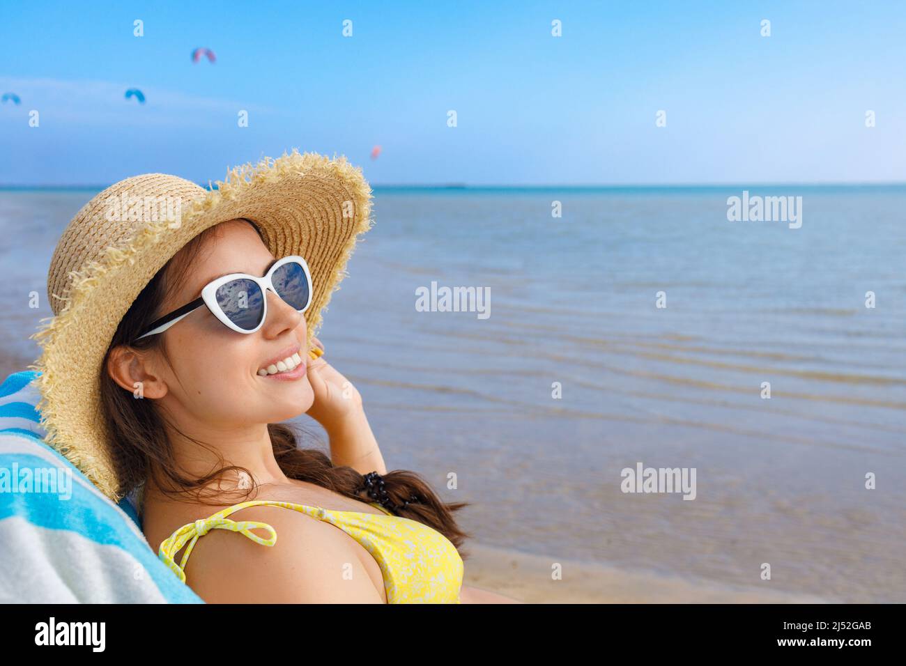 ritratto di donna sorridente in cappello di paglia e occhiali da sole rilassante su lettino da sole Foto Stock