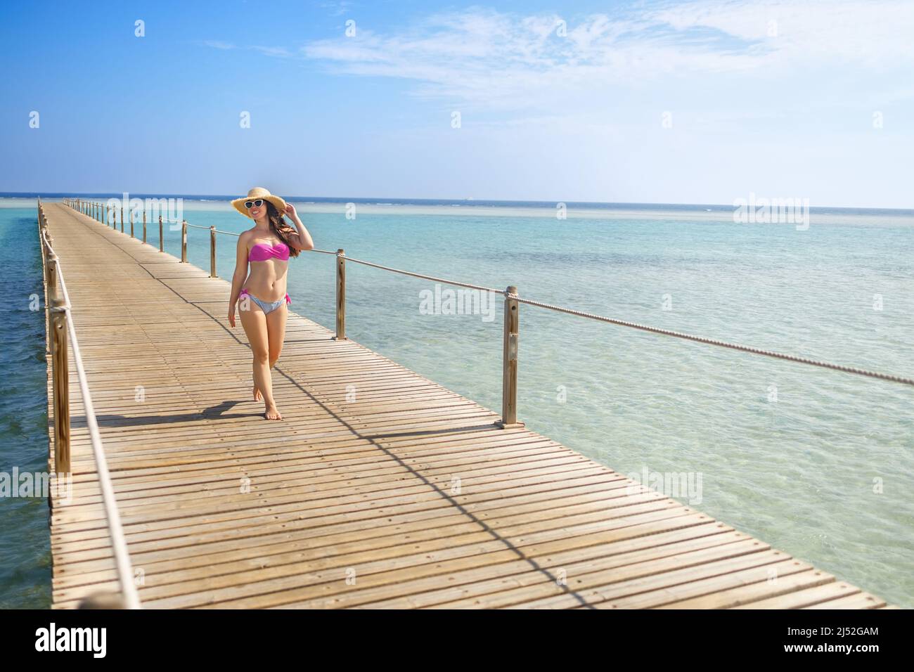 giovane donna sorridente in cappello di paglia che cammina sul pontile di legno Foto Stock