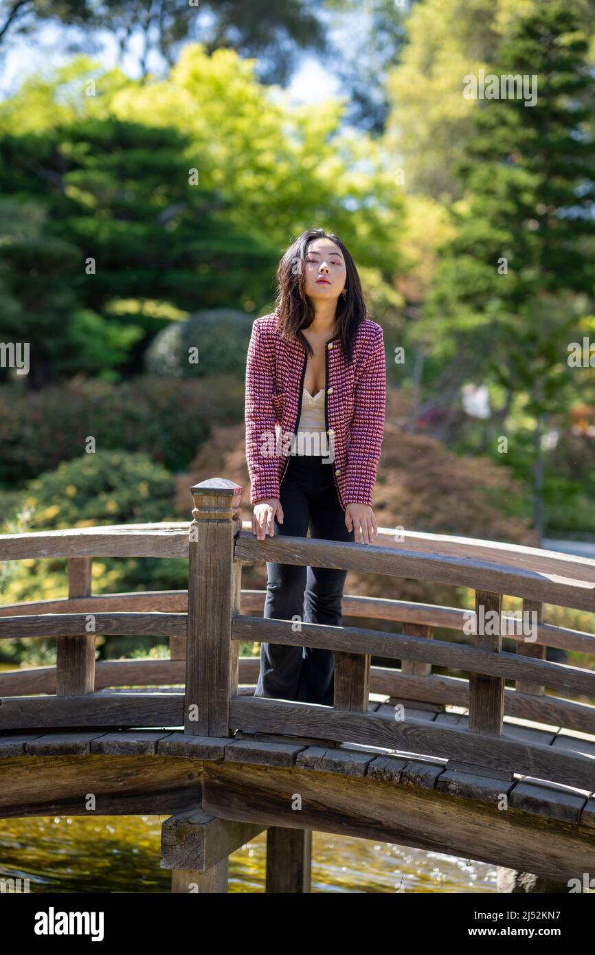Giovane donna in abiti casual su un ponte su un laghetto giapponese Koi Foto Stock
