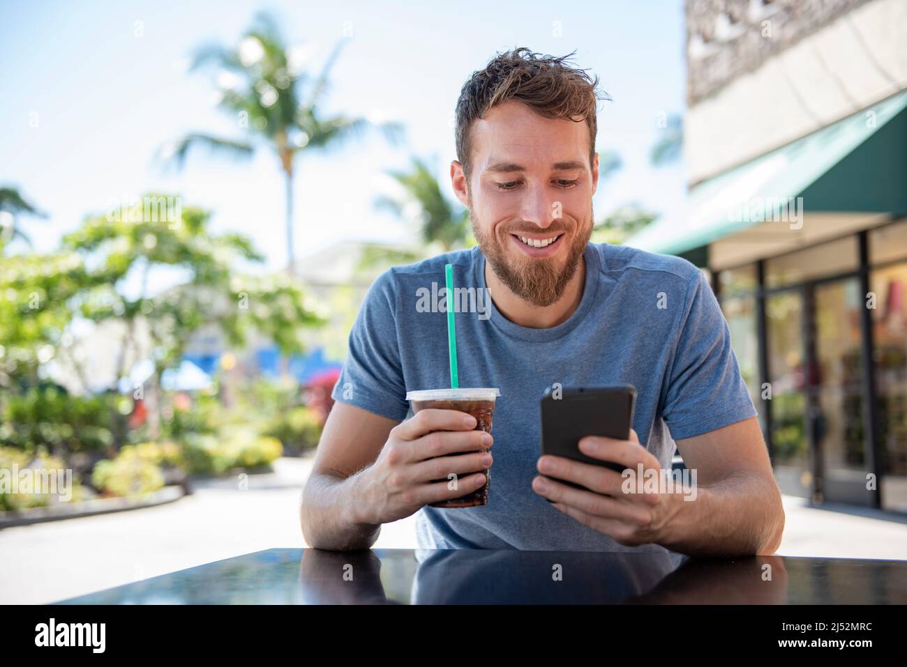 App per telefono giovane uomo che utilizza il dispositivo tecnologico che tiene il cellulare al caffè SMS con messaggi app sms bere caffè in estate. Bella giovane casual Foto Stock