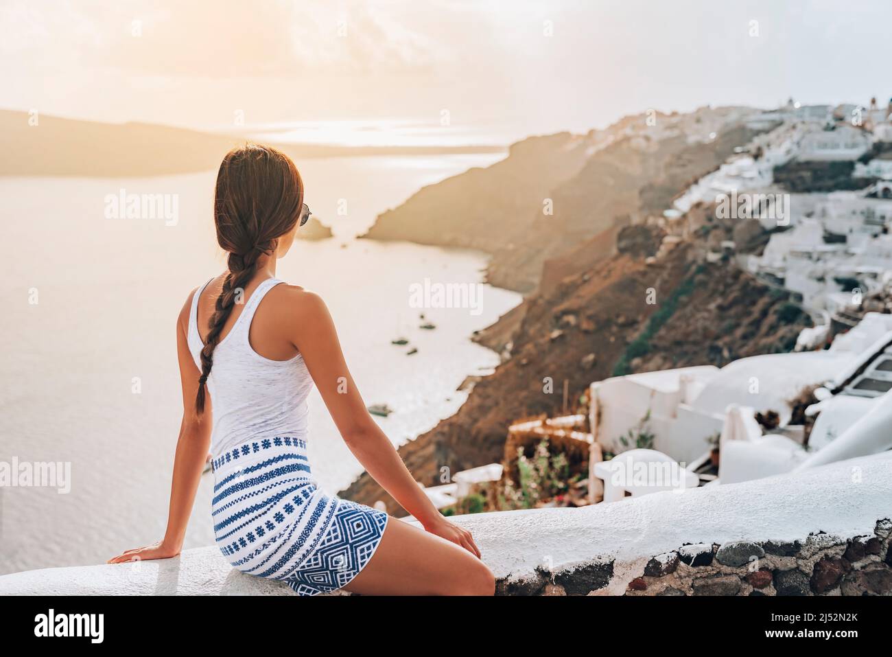 Grecia viaggio di lusso viaggio turistico donna guardare il tramonto da Santorini isola rilassarsi a vista mare Mediterraneo dalla costa dell'isola greca. Europa Foto Stock